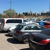 Amplio aparcamiento gratuito en el aeropuerto de Barcelona, con coches de diversos colores y modelos bajo un cielo azul.