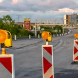 Una hilera de postes con luces naranjas intermitentes y marcas rojas y blancas, una señal de balizamiento, guía el tráfico en una carretera en construcción.