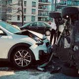 Dos coches involucrados en un accidente. Uno blanco, con el capó destrozado. El otro, volcado, muestra un siniestro total.