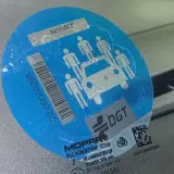 Pegatina azul con siluetas de personas y un coche, indicando la **señal v26**. Muestra un código de barras y el logo de DGT.