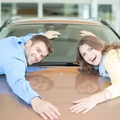 Pareja feliz abraza su nuevo coche, demostrando que se puede poner un coche a nombre de dos personas.
