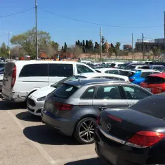 Amplio aparcamiento gratuito en el aeropuerto de Barcelona, con coches de diversos colores y modelos bajo un cielo azul.