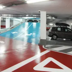 Estacionamiento subterráneo con señalización de salida y flechas en el suelo. Un coche oscuro con portaequipajes bsm flos i calcat.