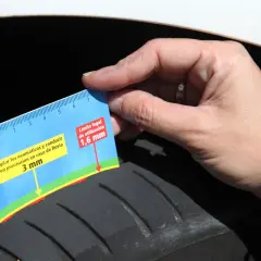 Mano mide la profundidad del dibujo de un neumático con una regla. Indica 3 mm y el límite legal de 1,6 mm, sugiriendo revisar la fecha caducidad neumáticos.