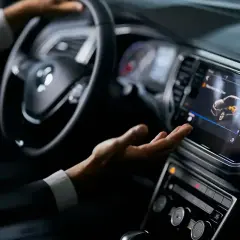 Mano interactuando con la pantalla táctil de un coche, mostrando el futuro de los coches autónomos.