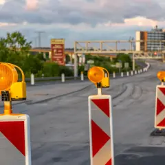 Una hilera de postes con luces naranjas intermitentes y marcas rojas y blancas, una señal de balizamiento, guía el tráfico en una carretera en construcción.