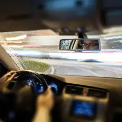 Conduciendo de noche bajo la lluvia, las luces de la carretera se difuminan. El conductor, con gafas, se refleja en el retrovisor, mostrando que es el ASR de un coche.