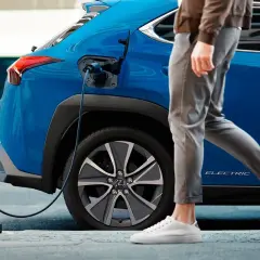 Un coche azul eléctrico se carga mientras una persona camina. Así es un phev que es, híbrido enchufable.