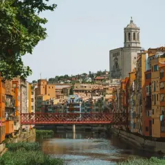 Casas de colores junto al río Onyar y el puente de piedra roja. La catedral se alza al fondo. Una vista encantadora para saber cómo llegar a Girona.