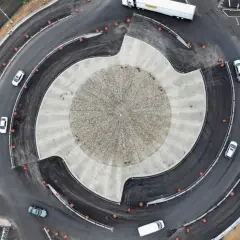 Vista aérea de una turbo rotonda en construcción, con coches circulando y un rodillo amarillo trabajando.