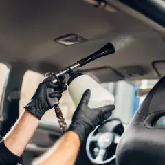 Man con guantes negros usa una pistola de espuma para limpiar el techo del coche.