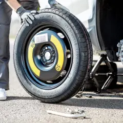 Persona con guantes cambia una rueda de repuesto, esencial ya que es obligatorio llevar rueda de repuesto. El coche está en un gato.