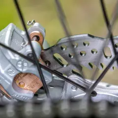 Primer plano de un freno de disco de bicicleta con pastillas de freno gastadas. El disco metálico muestra signos de uso, y las pastillas de freno están desgastadas.