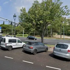 Coches aparcados en zonas blancas de Barcelona, junto a un parque y una carretera.
