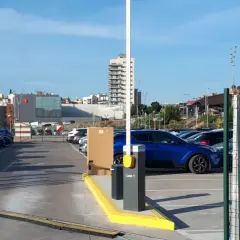 Amplio parking BSM Vall d'Hebron con coches aparcados y barrera de acceso. Edificios modernos y colinas al fondo.