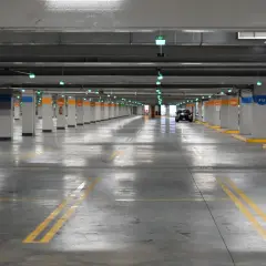 Estacionamiento subterráneo con luces verdes, columnas numeradas y un coche negro. Líneas amarillas marcan los espacios. ¡Encuentra tu lugar de parking gratis!