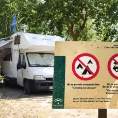 Una autocaravana blanca está aparcada junto a un cartel que prohíbe acampar y aparcar caravanas de noche.