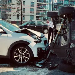 Dos coches involucrados en un accidente. Uno blanco, con el capó destrozado. El otro, volcado, muestra un siniestro total.