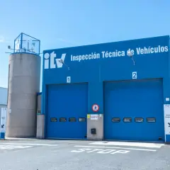 Edificio azul de ITV con dos puertas de garaje. Un coche listo para pasar la primera ITV.