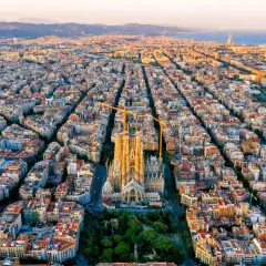Vista aérea de Barcelona al atardecer, con la Sagrada Familia como punto focal. Las grúas de construcción rodean la basílica, símbolo de la ciudad.