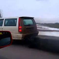 Un coche emite una densa nube de humo negro mientras circula por una carretera nevada.