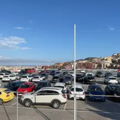 Amplio aparcamiento de coches en bsm Sant Genís, con la ciudad al fondo bajo un cielo azul.