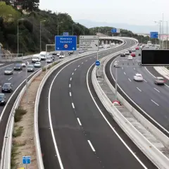 Autopista con varios carriles, incluyendo un carril Vao, con tráfico de coches y furgonetas. Señales de tráfico indican direcciones.