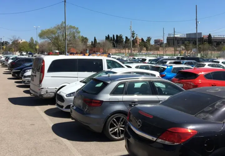 Amplio aparcamiento gratuito en el aeropuerto de Barcelona, con coches de diversos colores y modelos bajo un cielo azul.