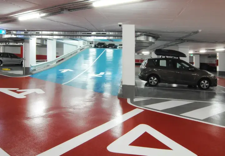 Estacionamiento subterráneo con señalización de salida y flechas en el suelo. Un coche oscuro con portaequipajes bsm flos i calcat.