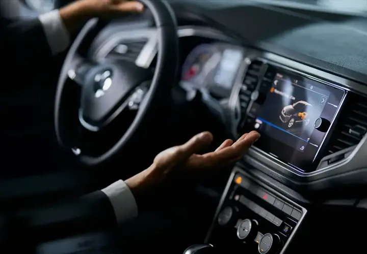 Mano interactuando con la pantalla táctil de un coche, mostrando el futuro de los coches autónomos.