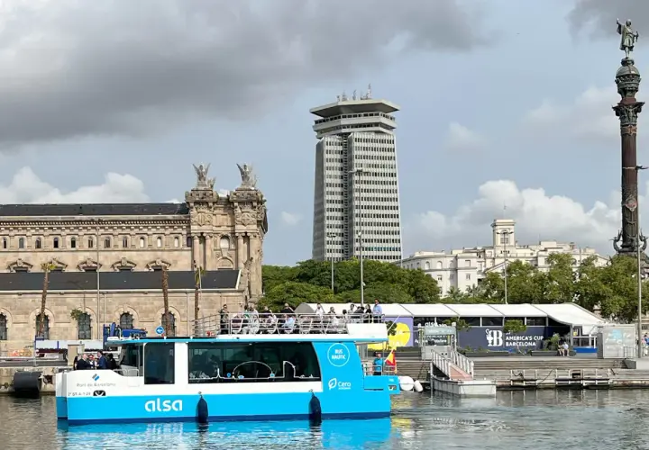 Barco turístico azul navega en el hafen Barcelona, con edificios históricos y modernos de fondo.