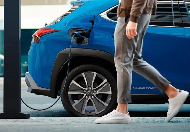 Un coche azul eléctrico se carga mientras una persona camina. Así es un phev que es, híbrido enchufable.