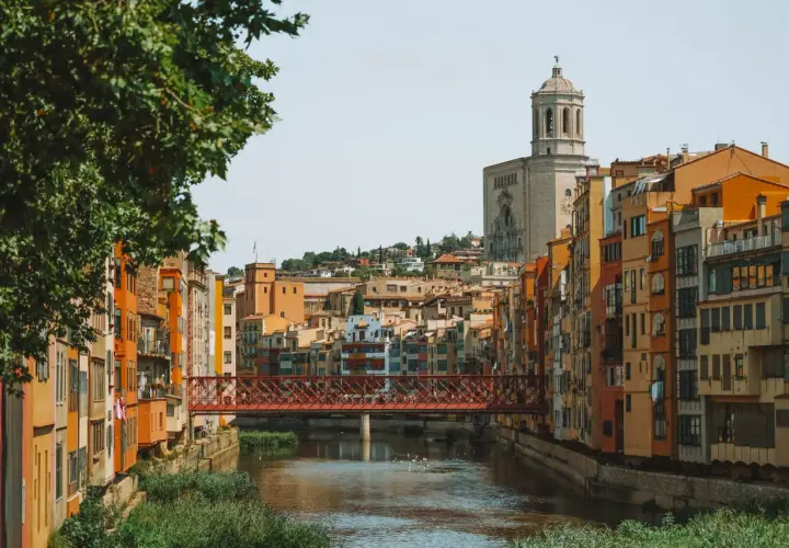 Casas de colores junto al río Onyar y el puente de piedra roja. La catedral se alza al fondo. Una vista encantadora para saber cómo llegar a Girona.