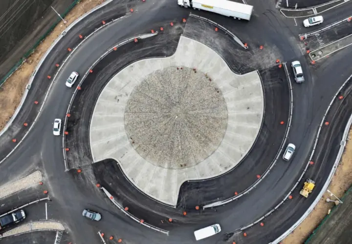 Vista aérea de una turbo rotonda en construcción, con coches circulando y un rodillo amarillo trabajando.