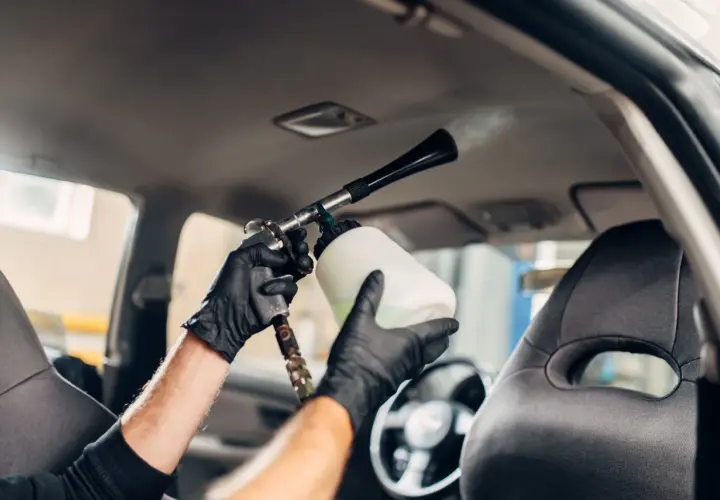 Man con guantes negros usa una pistola de espuma para limpiar el techo del coche.