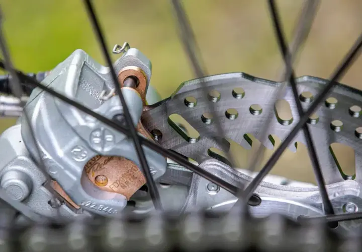 Primer plano de un freno de disco de bicicleta con pastillas de freno gastadas. El disco metálico muestra signos de uso, y las pastillas de freno están desgastadas.