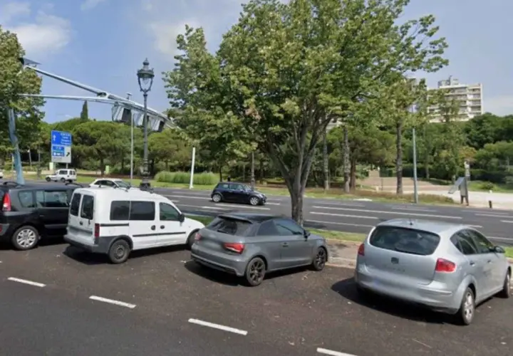 Coches aparcados en zonas blancas de Barcelona, junto a un parque y una carretera.