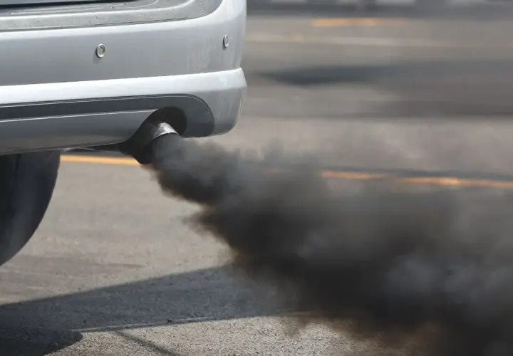 El tubo de escape de un coche emite humo negro denso, sugiriendo un fuerte olor a quemado de coche.
