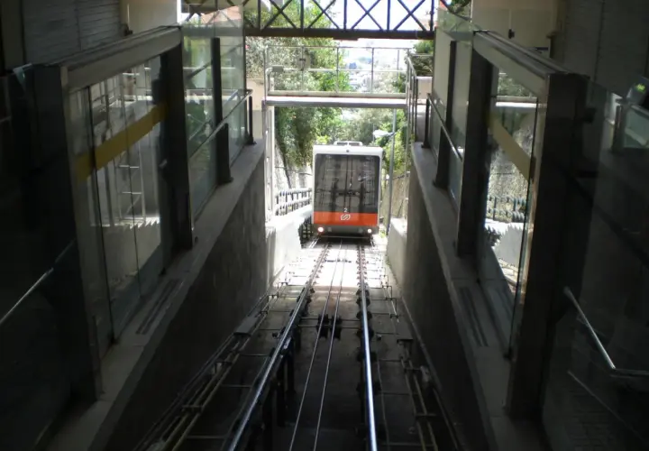 El funicular de Vallvidrera desciende por las vías entre estructuras de vidrio y hormigón, con vegetación al fondo.