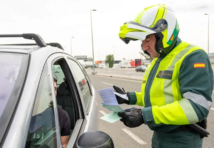 Agente de la Guardia Civil, con casco y chaleco reflectante, se acerca a un coche para entregar un documento. Parece que prescribe una multa.