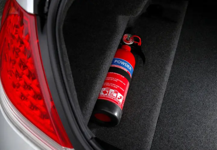 Extintor rojo en el maletero de un coche, listo para usar. Es obligatorio llevar extintor en el coche para tu seguridad.