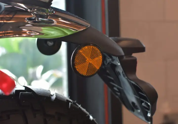 Detalle de una moto con un catadióptrico naranja que refleja la luz, aumentando la seguridad.