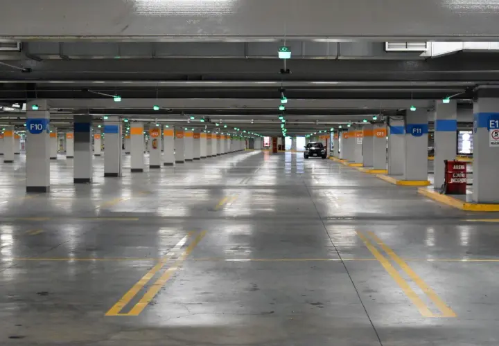 Estacionamiento subterráneo con luces verdes, columnas numeradas y un coche negro. Líneas amarillas marcan los espacios. ¡Encuentra tu lugar de parking gratis!
