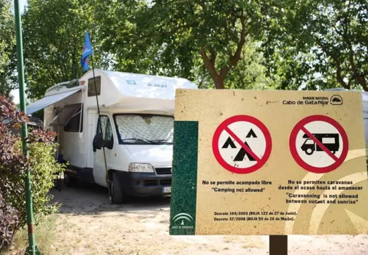 Una autocaravana blanca está aparcada junto a un cartel que prohíbe acampar y aparcar caravanas de noche.
