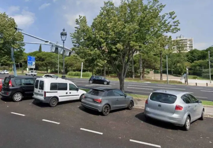 Varios coches aparcados en el parking del Hospital del Mar, con árboles y edificios al fondo.
