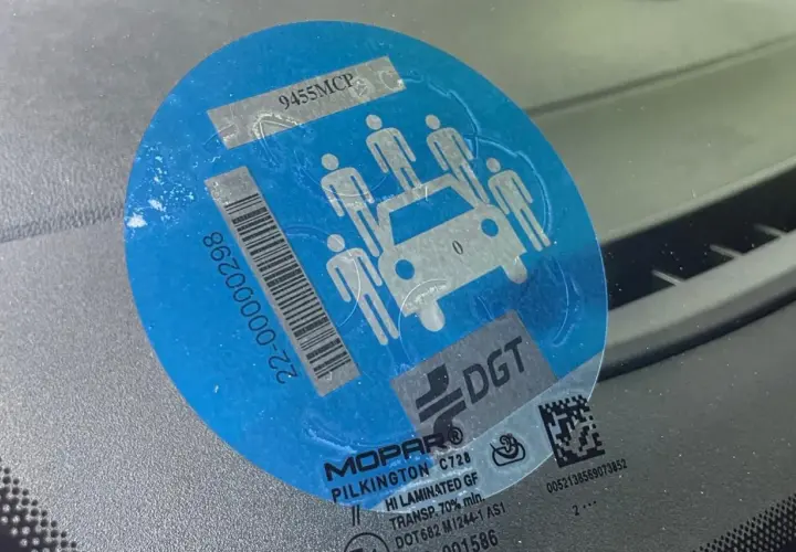 Pegatina azul con siluetas de personas y un coche, indicando la **señal v26**. Muestra un código de barras y el logo de DGT.