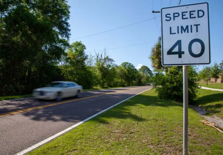 Señal de límite de velocidad de 40 en una carretera convencional. Un coche blanco pasa a gran velocidad.