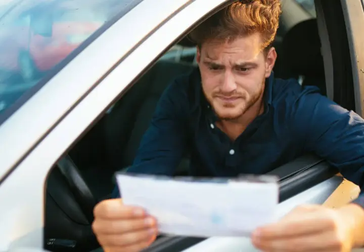 Hombre preocupado en su coche, mirando un papel que podría ser una multa. Se pregunta cuánto tarda en llegar una multa.