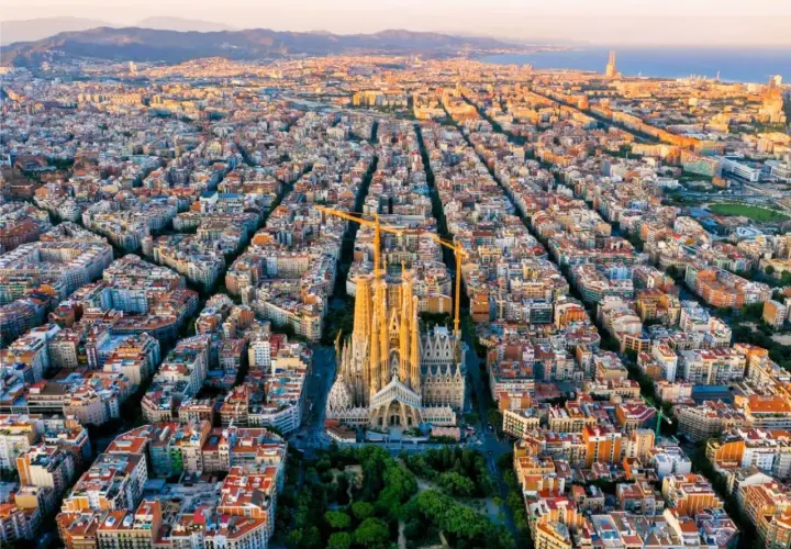 Vista aérea de Barcelona al atardecer, con la Sagrada Familia como punto focal. Las grúas de construcción rodean la basílica, símbolo de la ciudad.