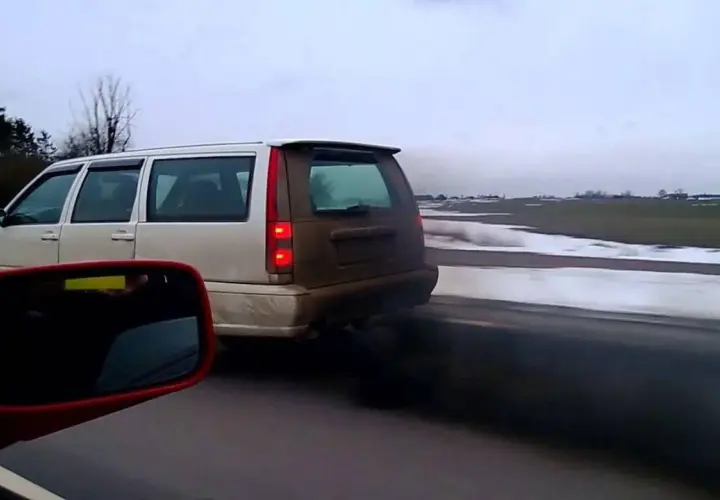 Un coche emite una densa nube de humo negro mientras circula por una carretera nevada.